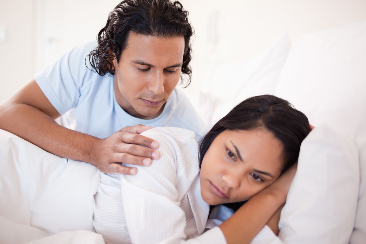 homem latino confortando mulher latina chateada na cama