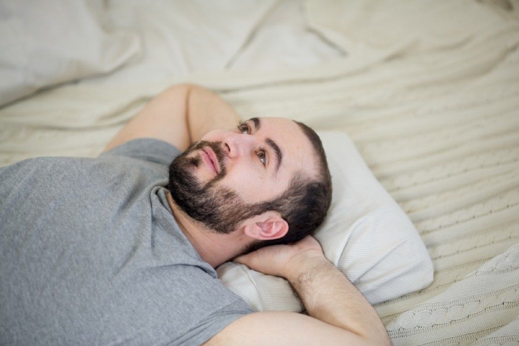 mladi bel moški na postelji z odprtimi očmi