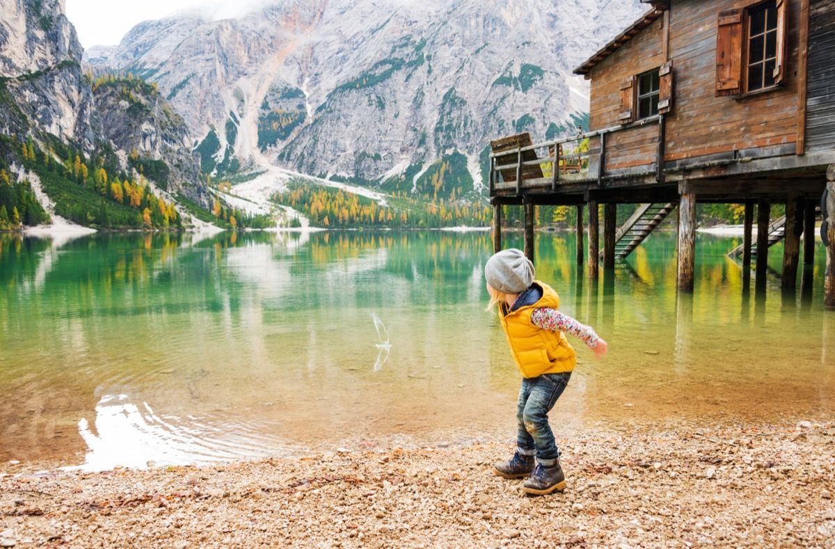 Маленькая девочка прыгает по камням на красивом озере