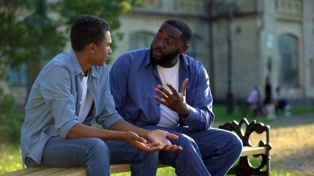 padre negro discutiendo con su hijo negro en un banco fuera