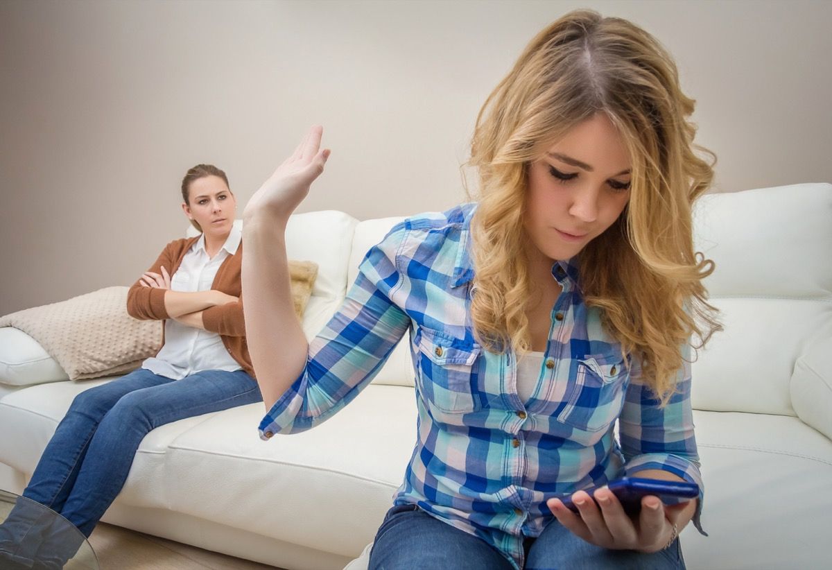Chica adolescente blanca enviando mensajes de texto y levantando la mano para ignorar a su madre en el fondo