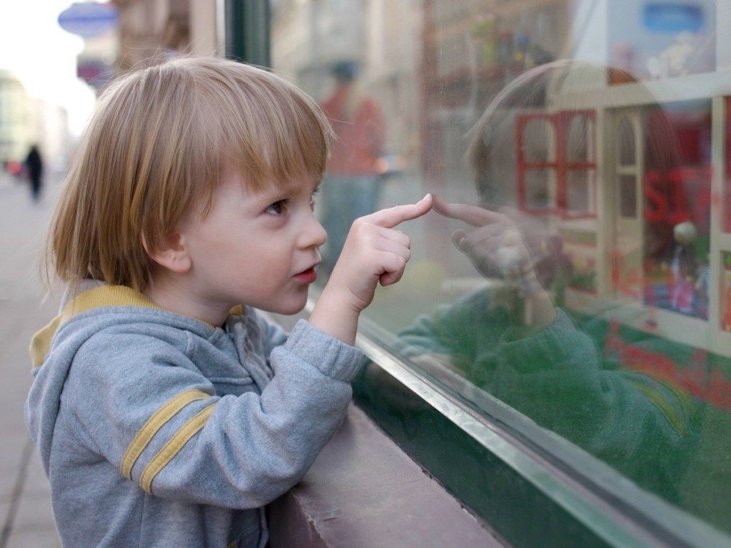 jaunas baltas berniukas, žvelgiantis į žaislų parduotuvės langą
