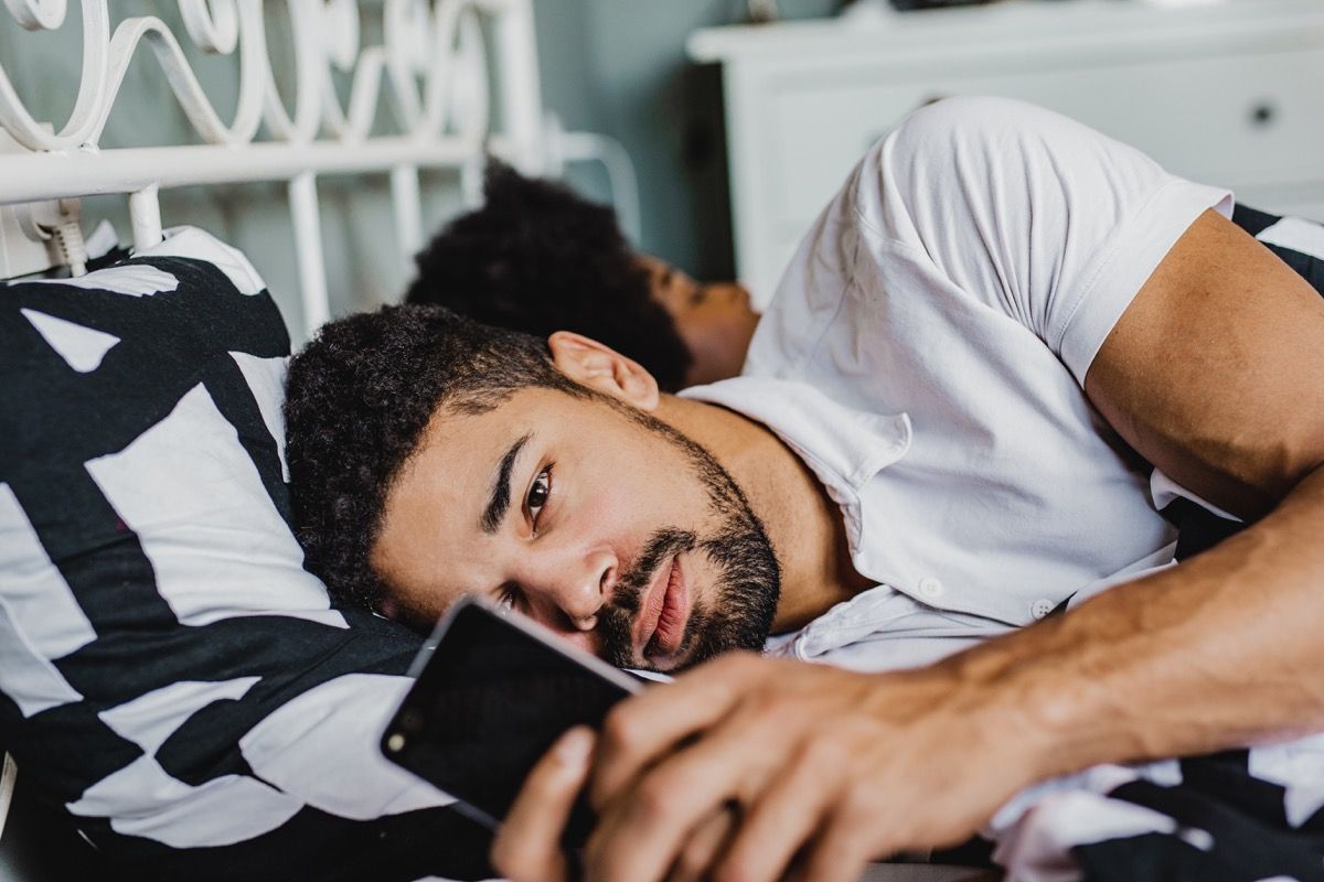Noored mehed lebavad oma tüdruksõbra kõrval voodis ja kasutavad nutitelefoni