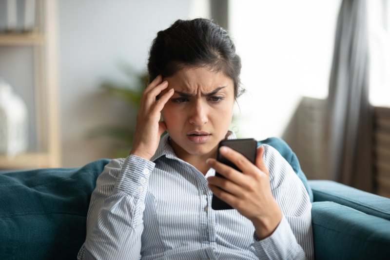   Млада жена гледа смартфона си със загрижено изражение на лицето.