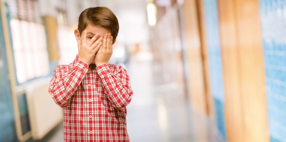 gutt dekker ansiktet i forlegenhet på skolegangen