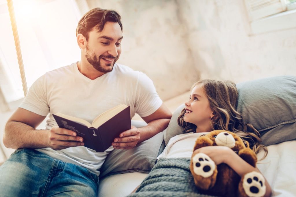 far lese bok til datter holder bamse i sengen