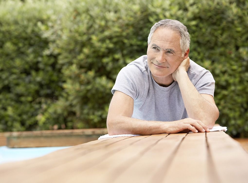 vanhempi valkoinen mies ajattelee istuessaan piknikpöydällä, puolikas hymy kasvoillaan