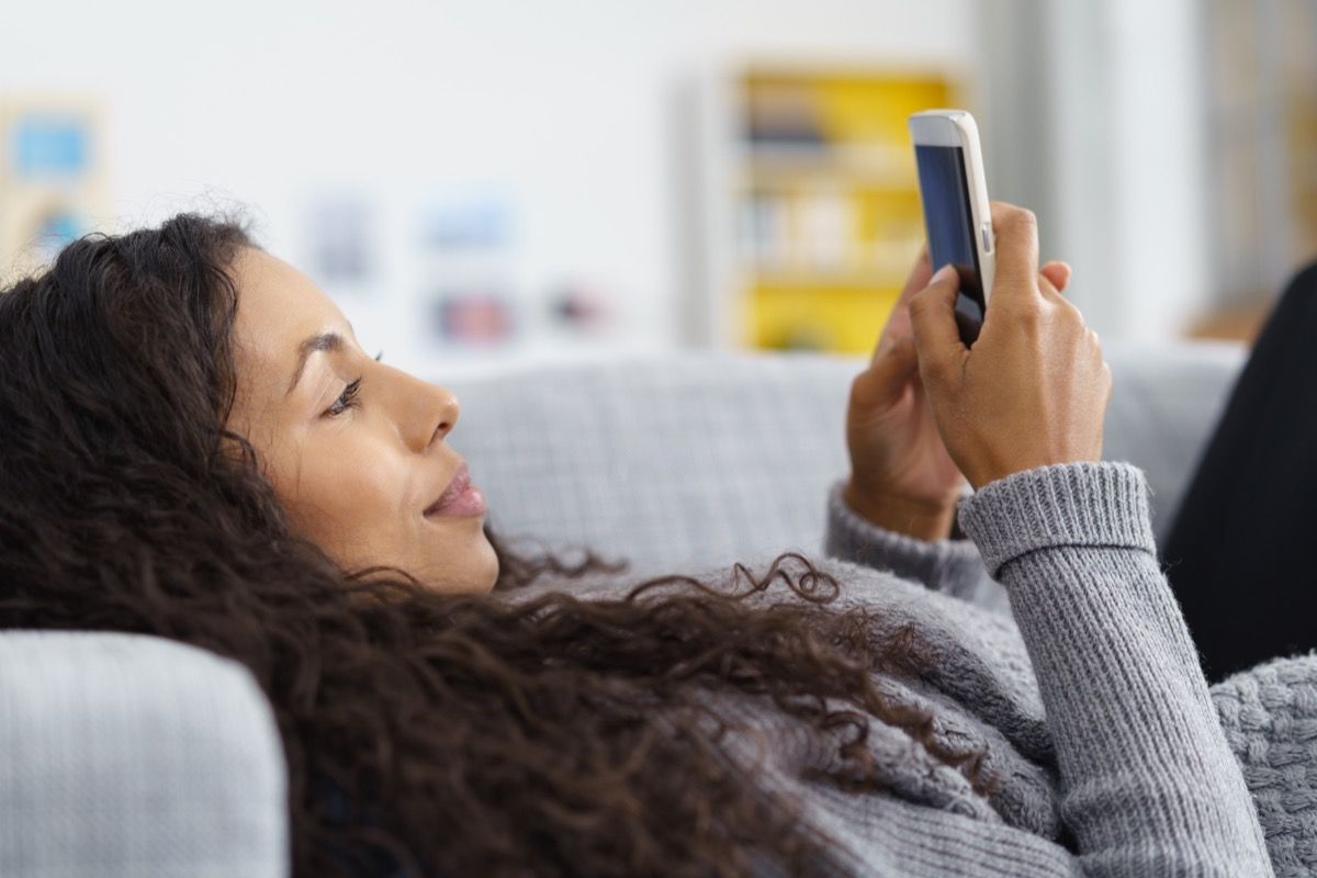 жена, изпращаща съобщения по мобилен телефон на дивана