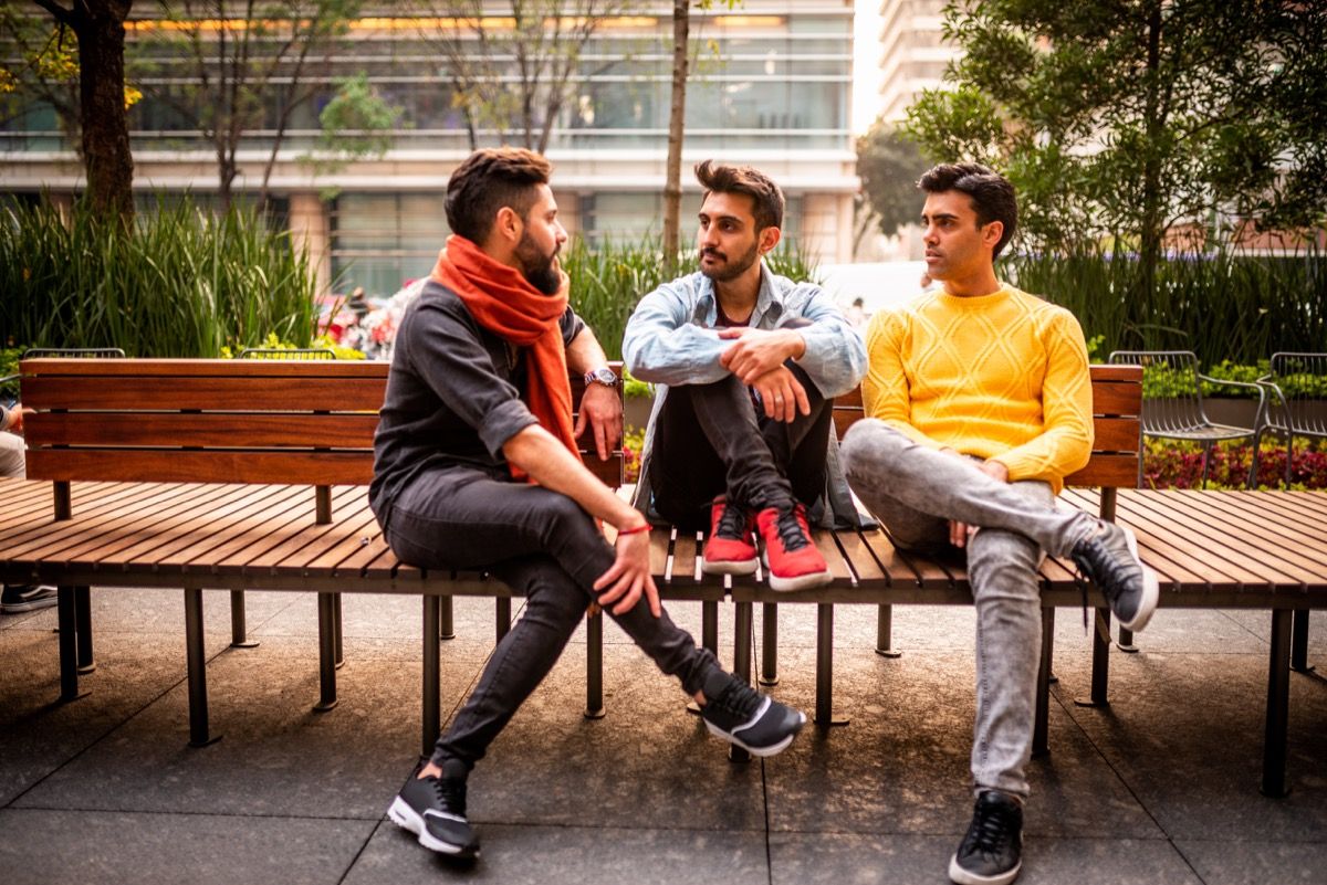 Grupo de tres amigos varones sentados en un banco en el barrio