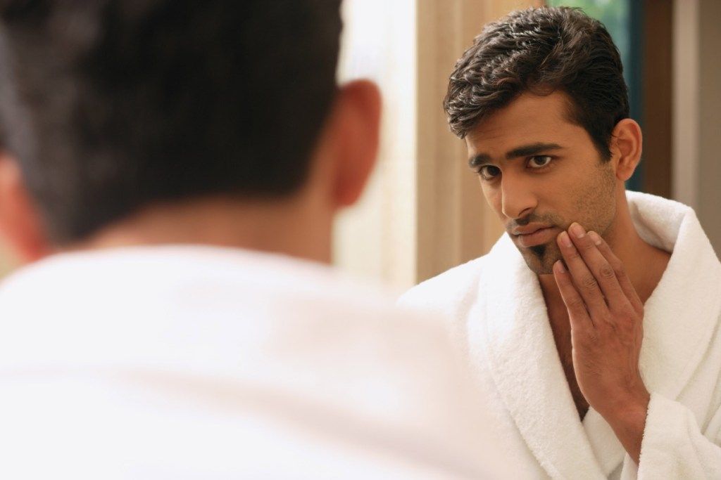 दर्पण में चेहरे का निरीक्षण करते युवा भारतीय पुरुष