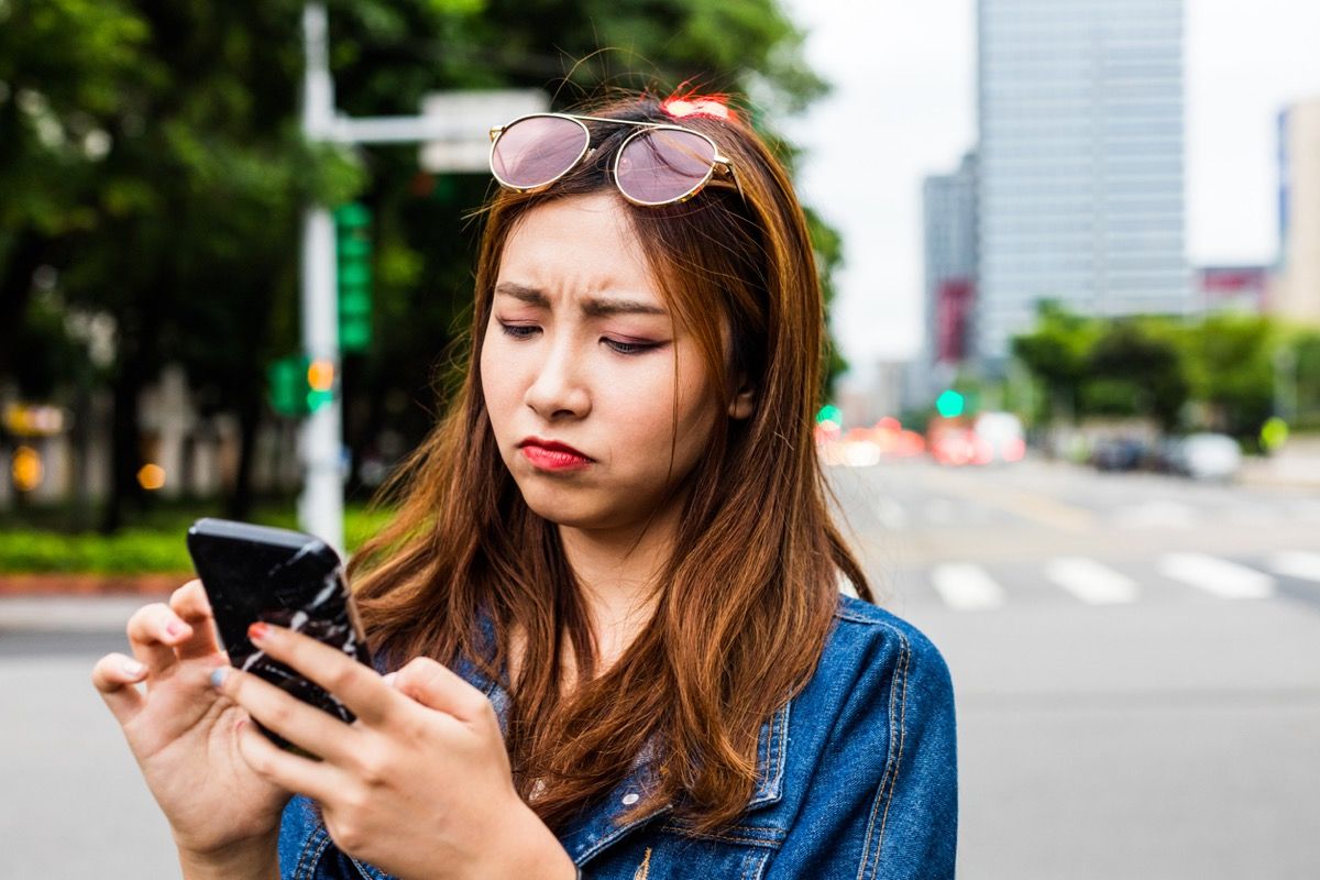 jauna Āzijas sieviete izskatās vīlušies, kamēr viņa lieto tālruni uz ielas