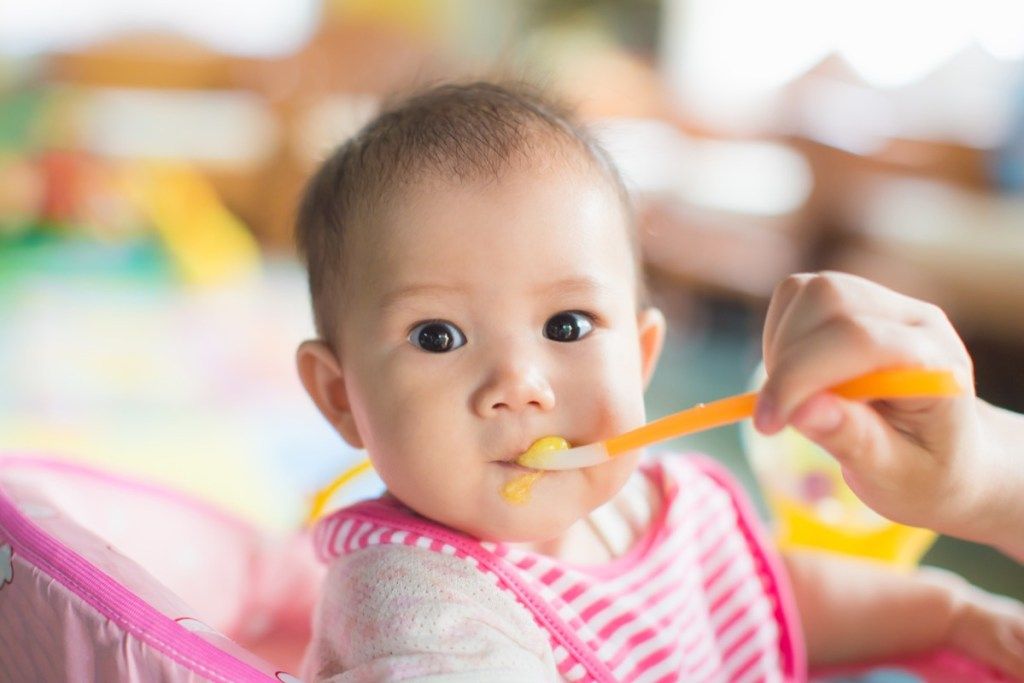 aasialainen vauva ruokitaan vaaleanpunaisella ruokalappulla