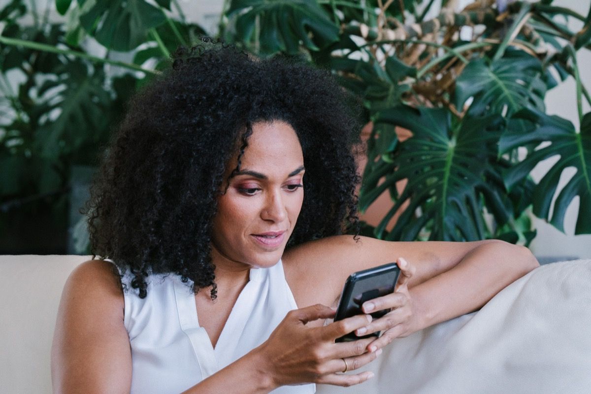 Femme sérieuse assise sur un canapé, envoyer des SMS à quelqu