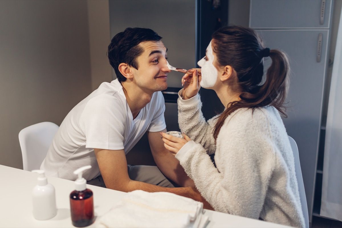 mulher aplicando uma máscara facial de argila no namorado
