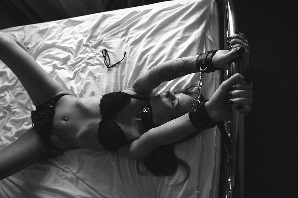 एक महिला बीडीएसएम खेल में एक बिस्तर पर हथकड़ी लगाती है - साक्षर