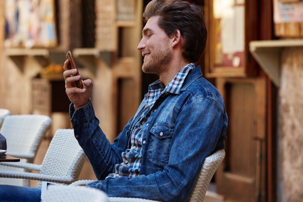 mies ulkona kahvilassa puhelimellaan, parhaat online-treffien avauslinjat