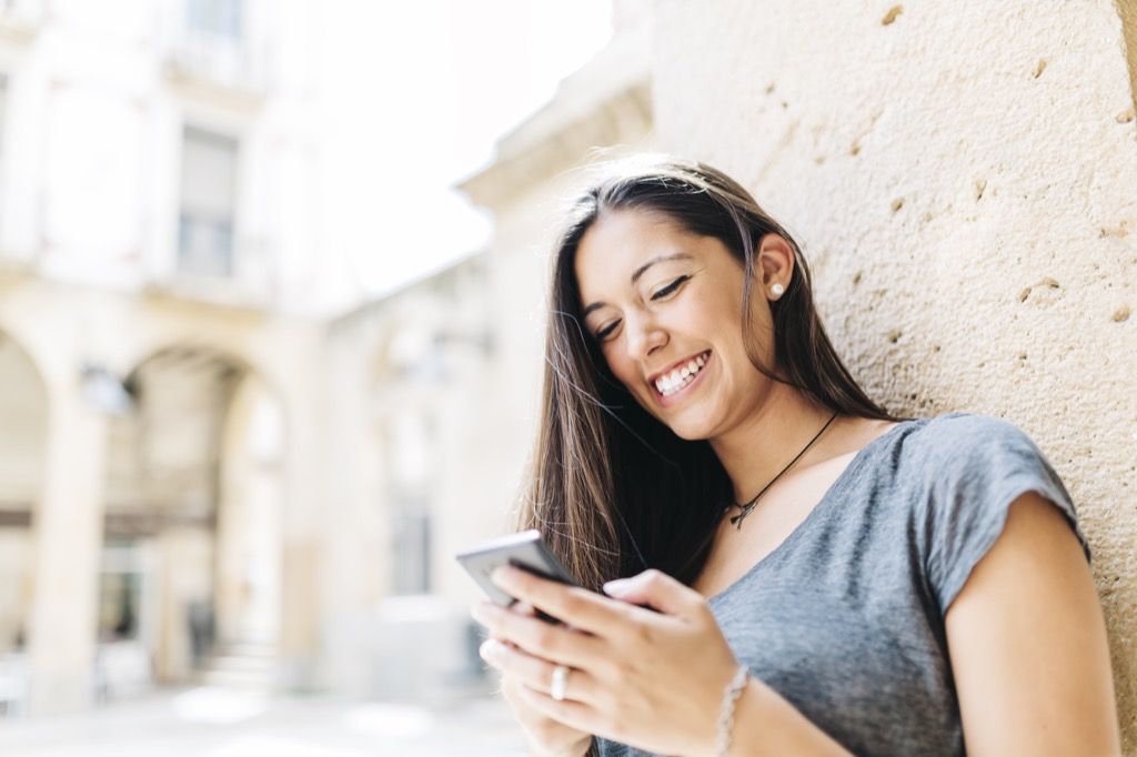nainen katselee puhelinta ja hymyilee, parhaat avauslinjat online-dating
