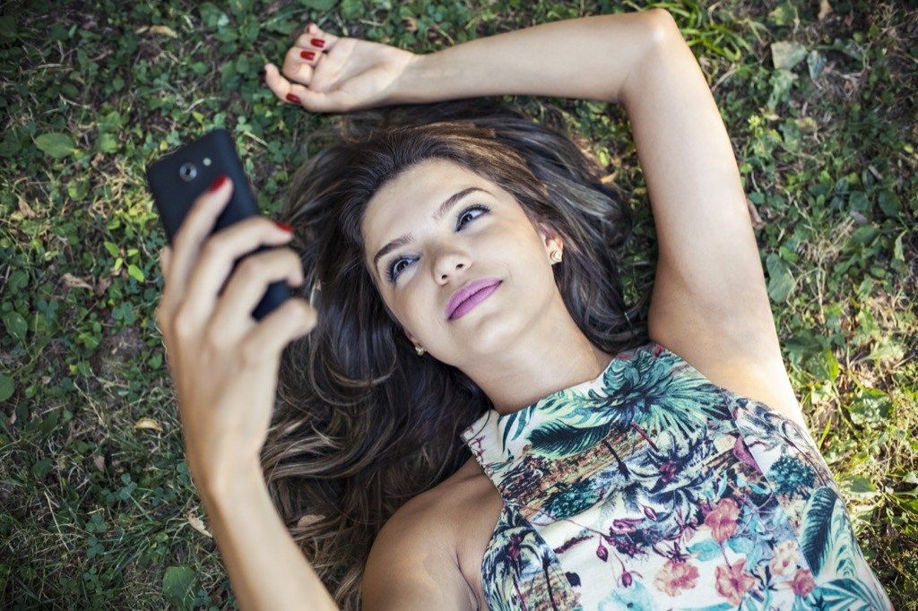 moteris, sėdinti žolėje savo telefone, kaip sužinoti, ar merginai tu patinki