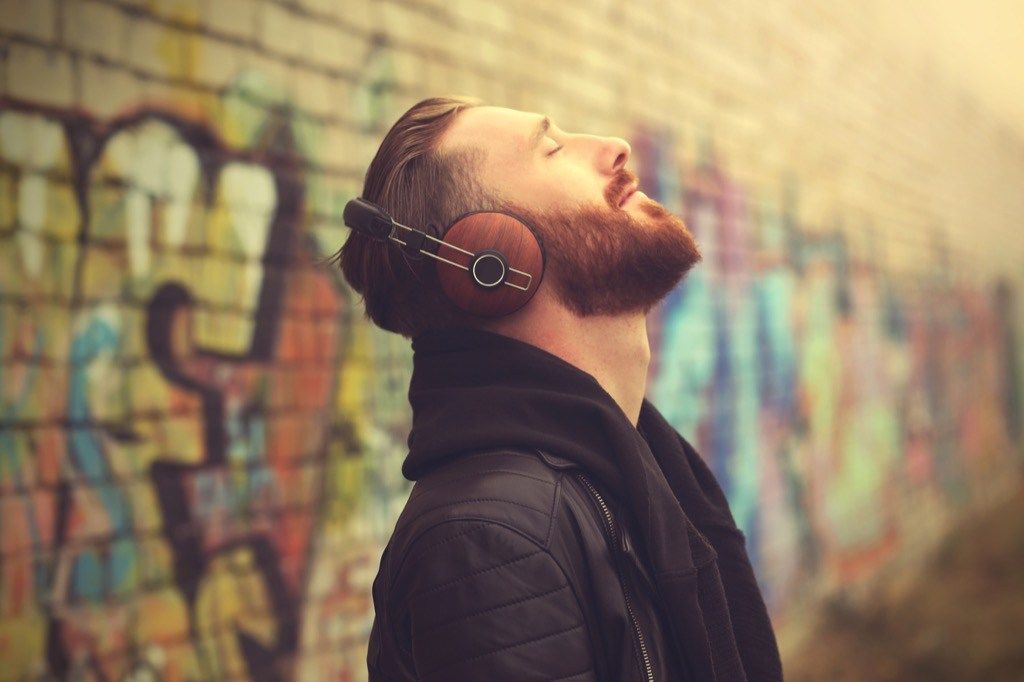 мъж, който слуша музика на слушалки отвън пред тухлена стена