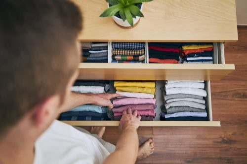   Organización y limpieza del hogar. Hombre preparando camisetas dobladas ordenadamente en el cajón.