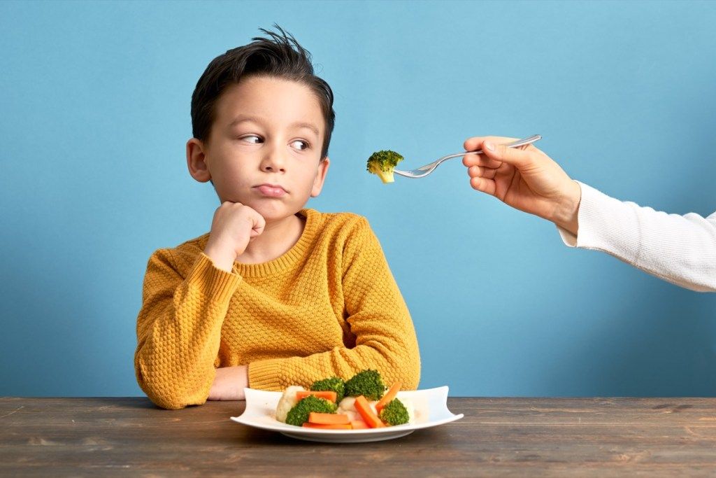 criança infeliz comendo brócolis