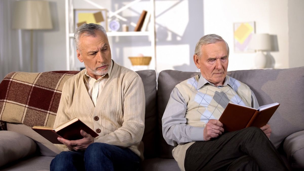 Dos amigos varones ofendido leyendo libros en el sofá en casa