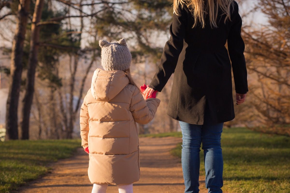 Mama ir dukra susikibusios rankomis vaikšto po parką rudenį, vyras išvyko būdamas nėščia