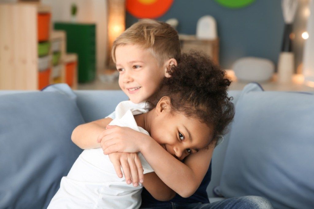 νεαρό κορίτσι και αγόρι που αγκαλιάζονται στον καναπέ, οι δεξιότητες που πρέπει να διδάσκουν οι γονείς στα παιδιά