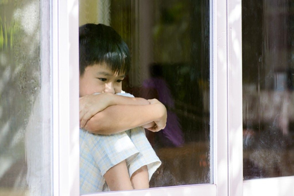 sarūgtināts skumjš zēns, kurš sēž pie loga un skatās pa to, prasmes, kas vecākiem jāmāca bērniem