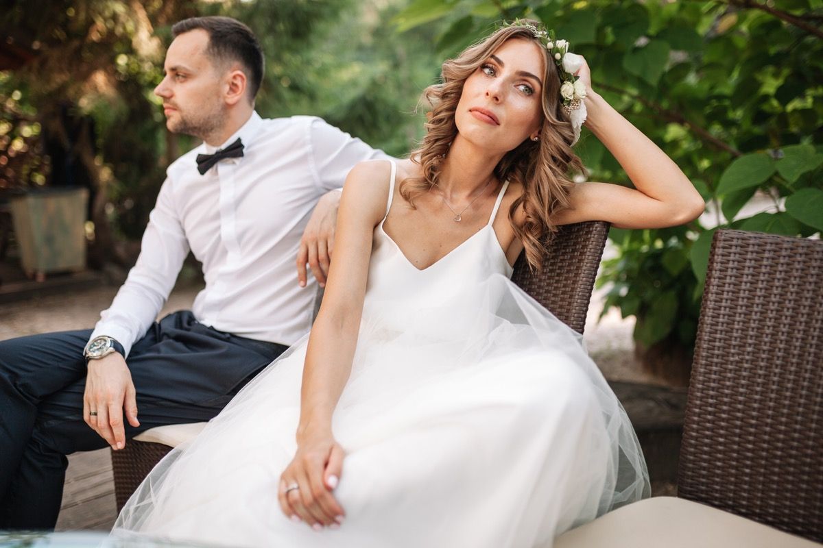 mujer blanca en vestido de novia mirando triste cerca de marido blanco al aire libre