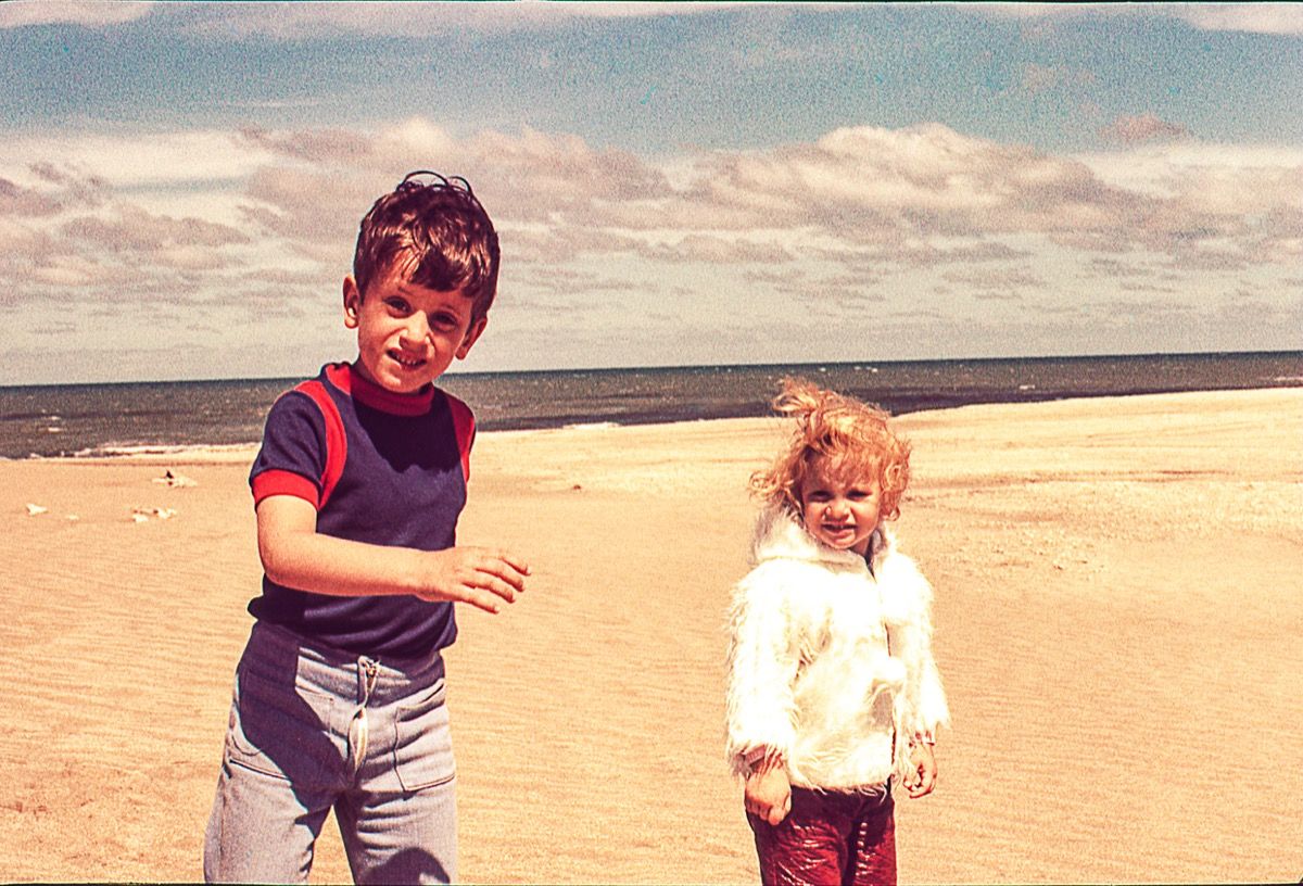 سردی کے دن ساحل سمندر پر اپنے بھائی کے ساتھ ایک خوبصورت سنہرے بالوں والی چھوٹی لڑکی کی ونٹیج تصویر۔