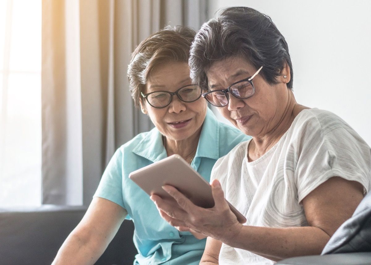 Azijos vyresnio amžiaus moterys, kurios atrodo kaip seserys dvynės, naudojančios mobilųjį skaitmeninį planšetinį kompiuterį