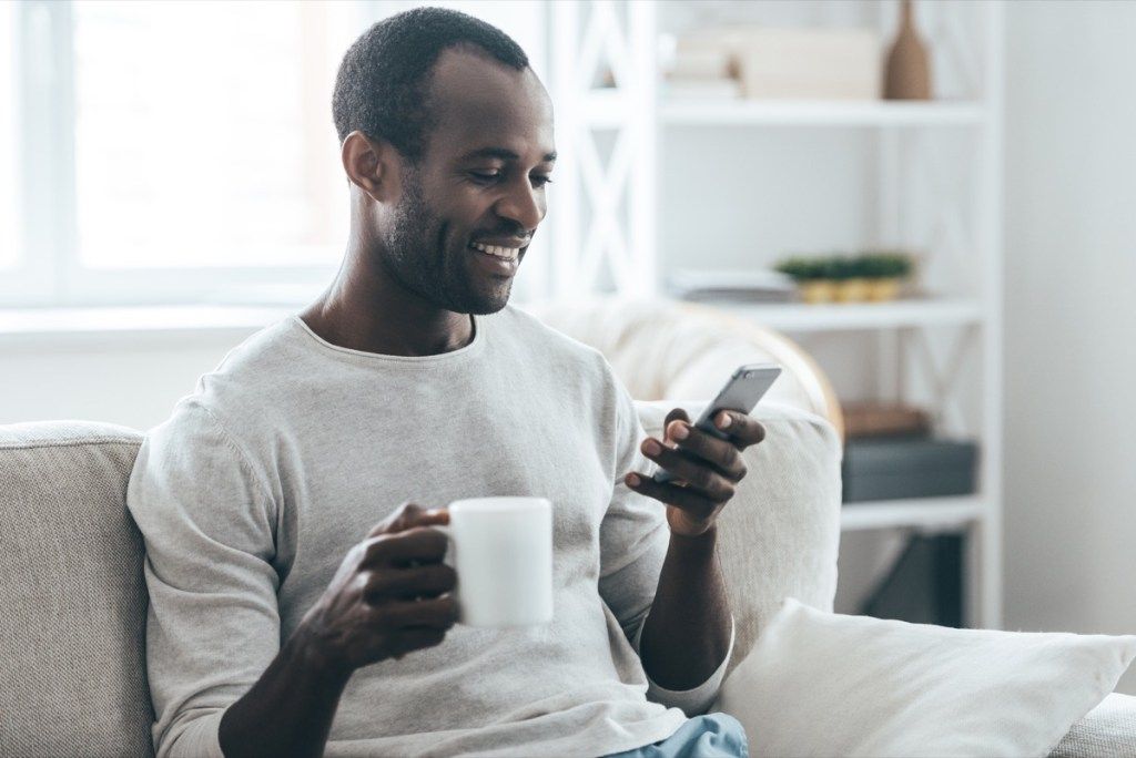 منتصف العمر رجل أسود الرسائل النصية على الأريكة مع فنجان الشاي