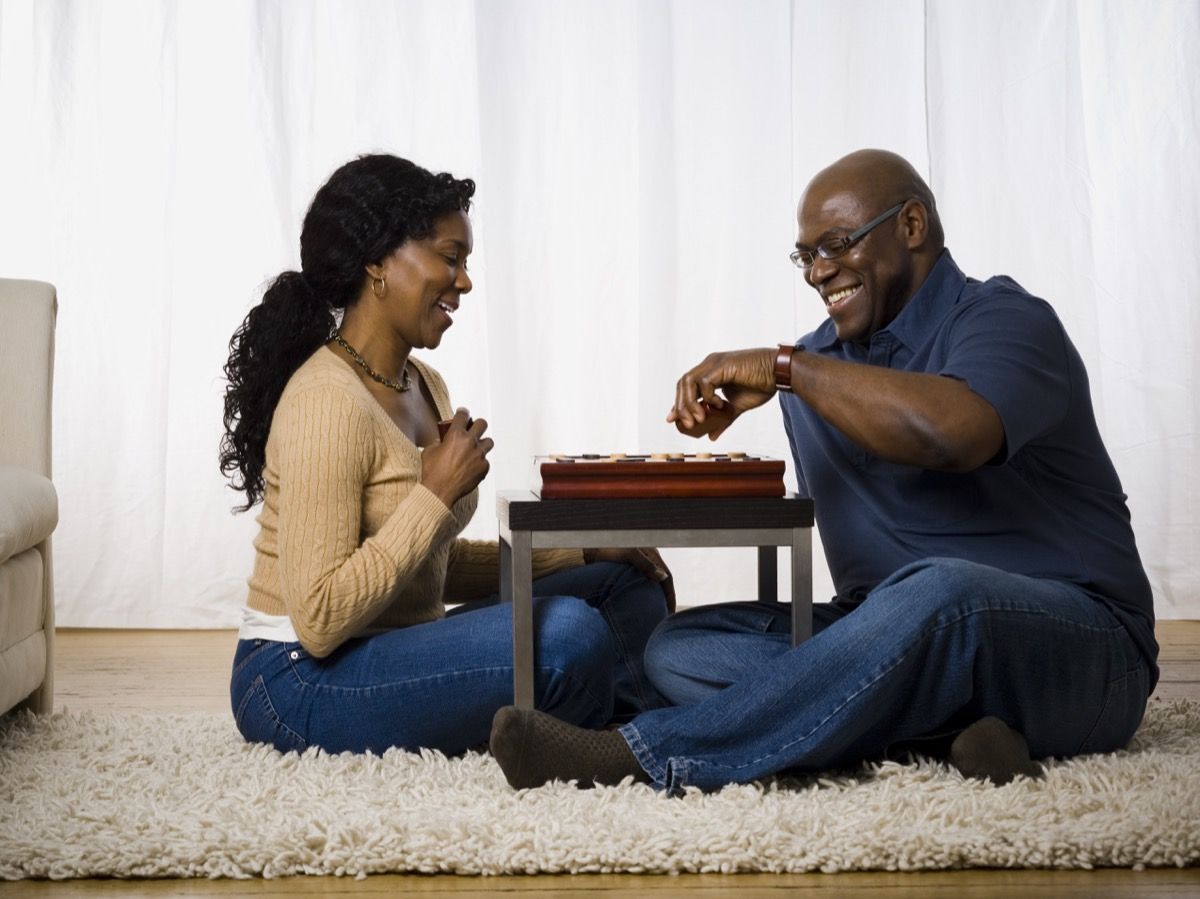 vidutinio amžiaus juoda pora žaidžianti stalo žaidimą ant grindų