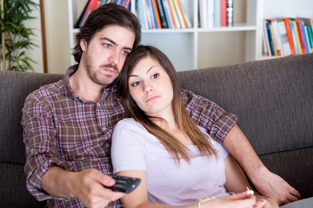 jauna balta pora kartu žiūri televizorių ir atrodo nuobodžiai