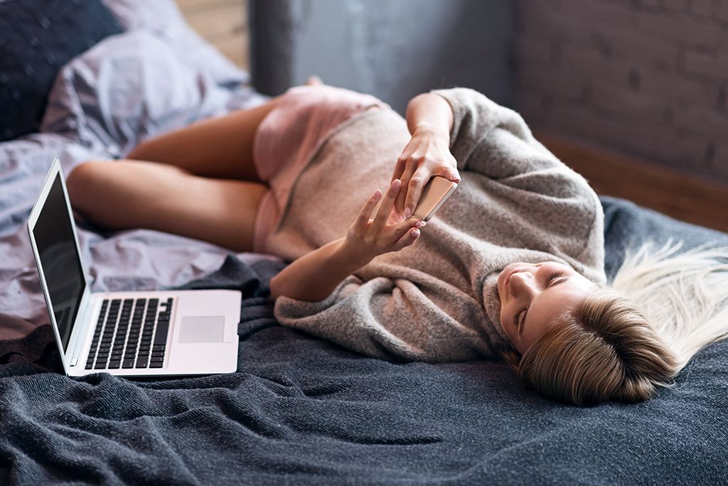 Mujer enviando mensajes de texto junto a una computadora portátil, siendo soltera