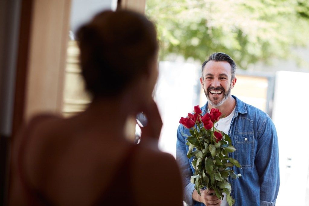 izrezani snimak atraktivnog zrelog muškarca koji iznenađuje svoju djevojku buketom ruža
