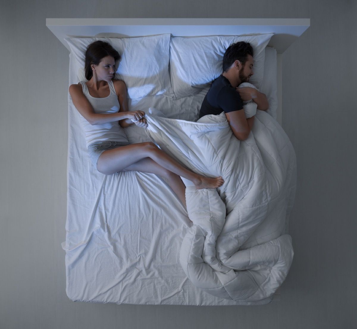 wanita kulit putih menarik selimut dari pria kulit putih yang memeganginya di tempat tidur