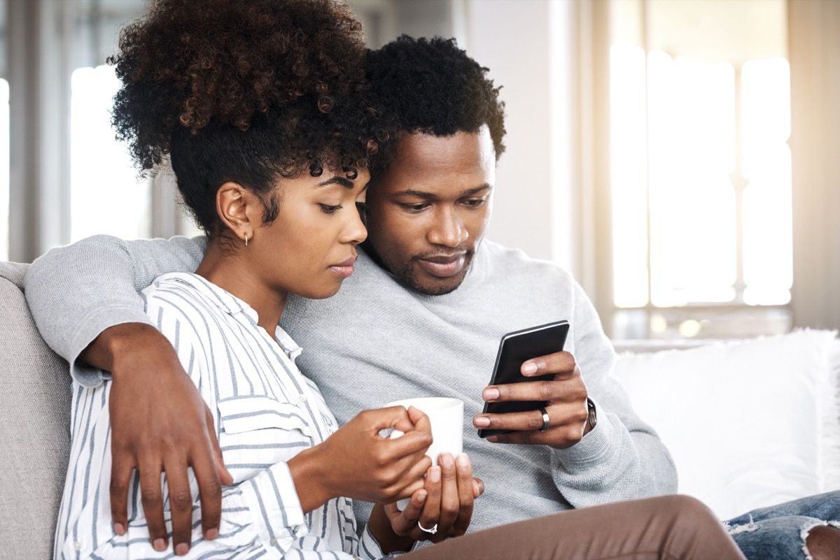 fiatal fekete nő kávéval és fekete fiatalember együtt nézi a telefont