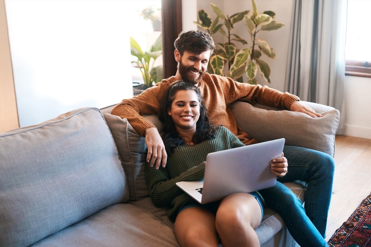 jaunas baltas vyras ir jauna balta moteris glaustosi ir šypsosi kartu nešiojamame kompiuteryje