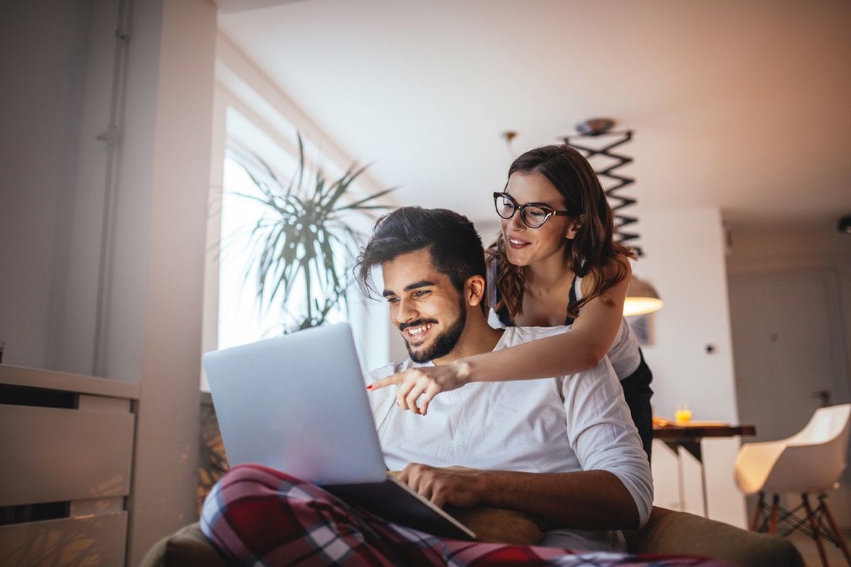 Mann lächelt am Laptop mit Frau, die auf Bildschirm hinter ihm zeigt