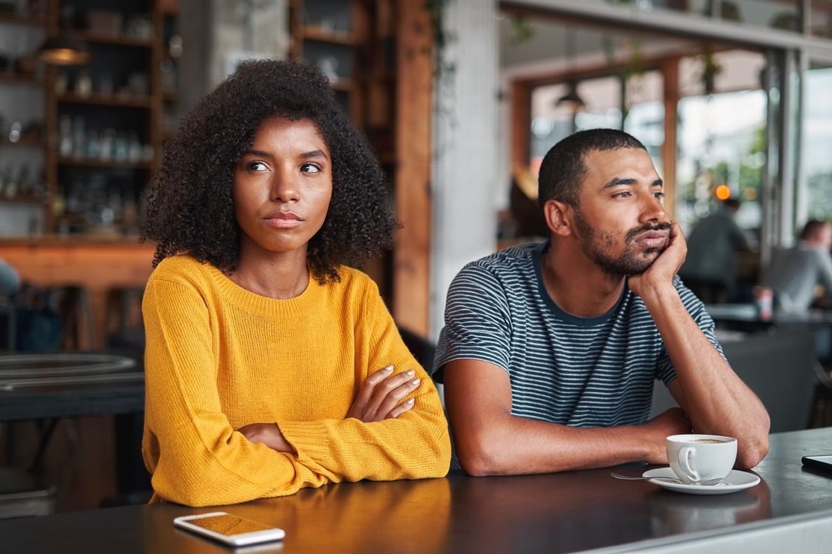 mladi crni par koji sjedi jedan do drugoga u kafiću i ne govori niti uspostavlja kontakt očima