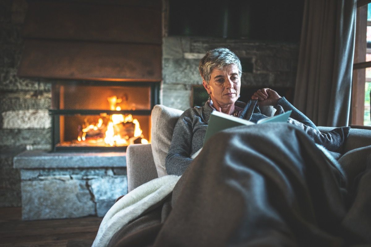starija bijelka koja čita knjigu pod pokrivačem kraj vatre