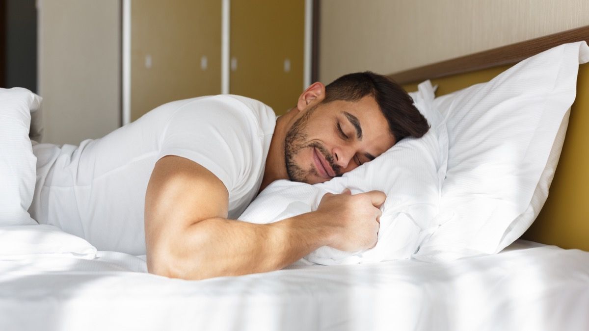 mladi latino muškarac koji se smiješi zatvorenih očiju dok leži na jastuku u krevetu