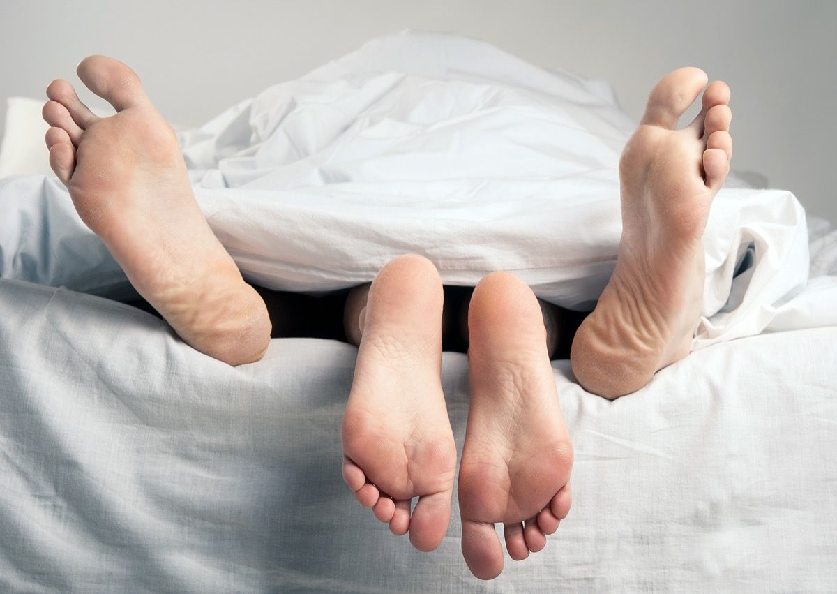 เท้าเปล่าของชายและหญิงมองออกมาจากใต้ผ้าปูที่นอนสีขาว