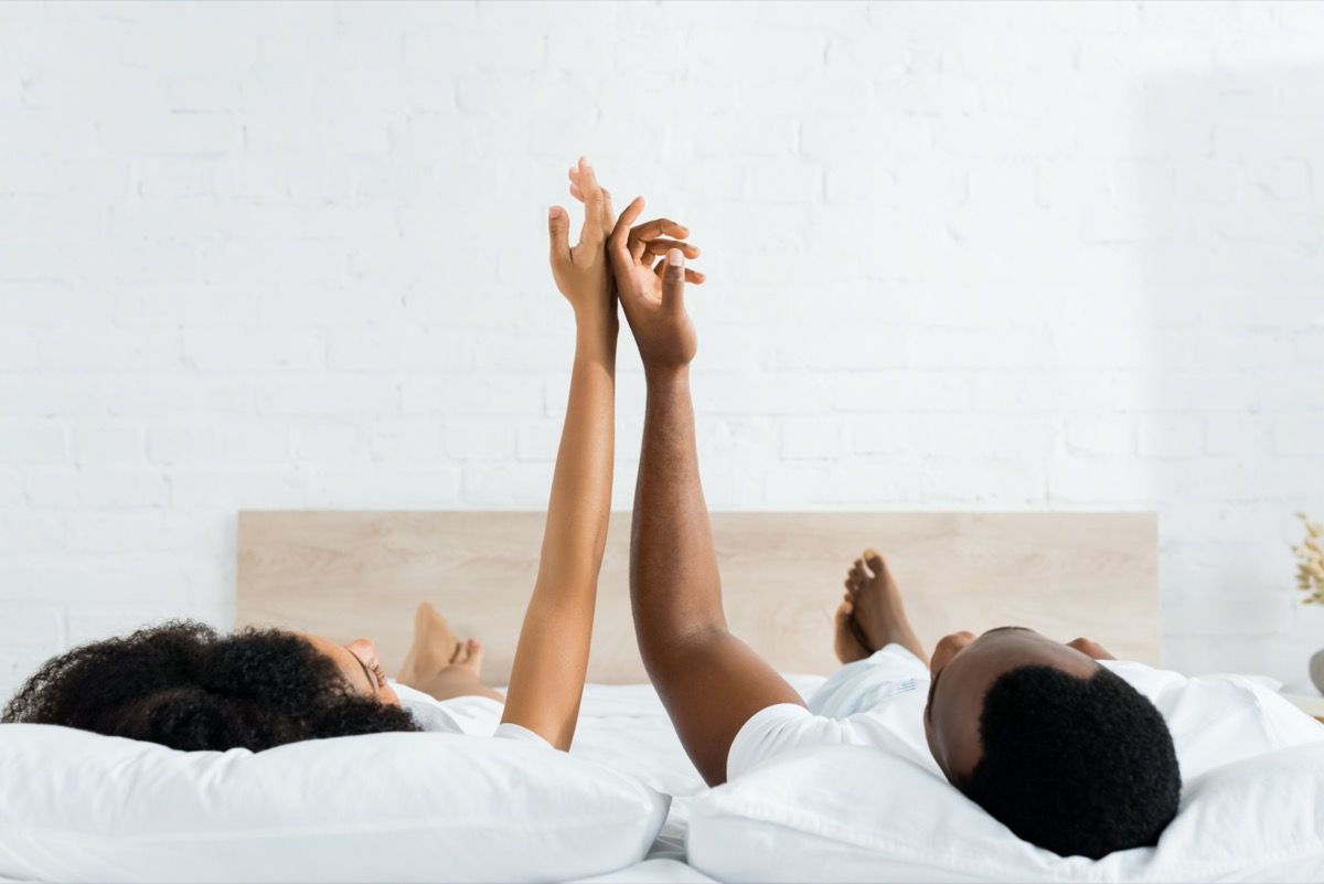 ชายและหญิงผิวดำนอนหงายอยู่บนเตียงสัมผัสมือ