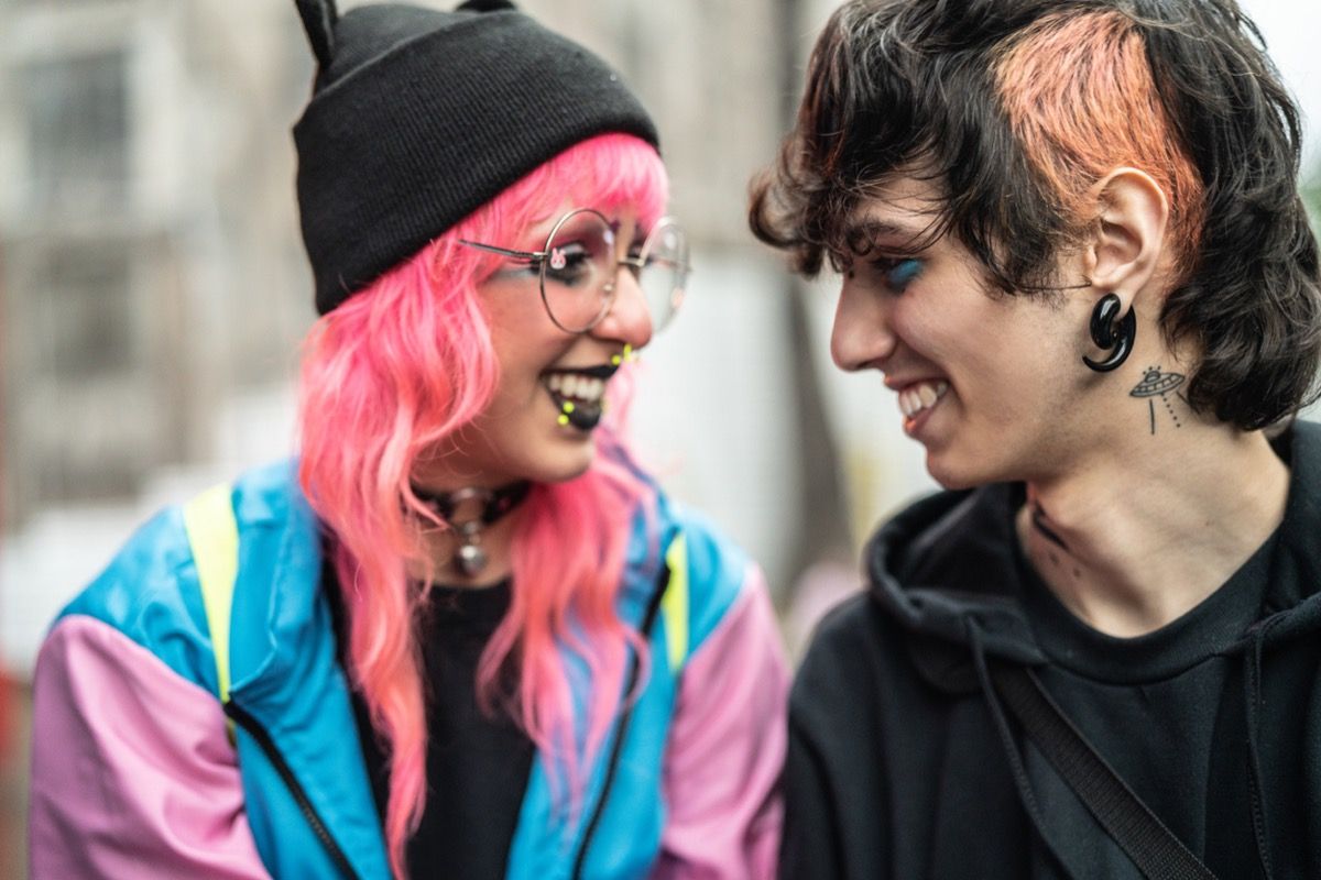 ung hvid kvinde med lyserødt hår smilende til ung hvid mand med piercinger