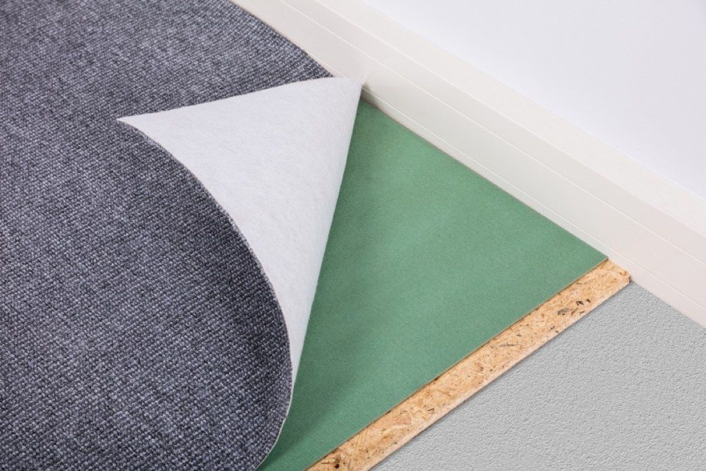 sivý koberec odlepujúci sa od zelenej podložky pod koberec
