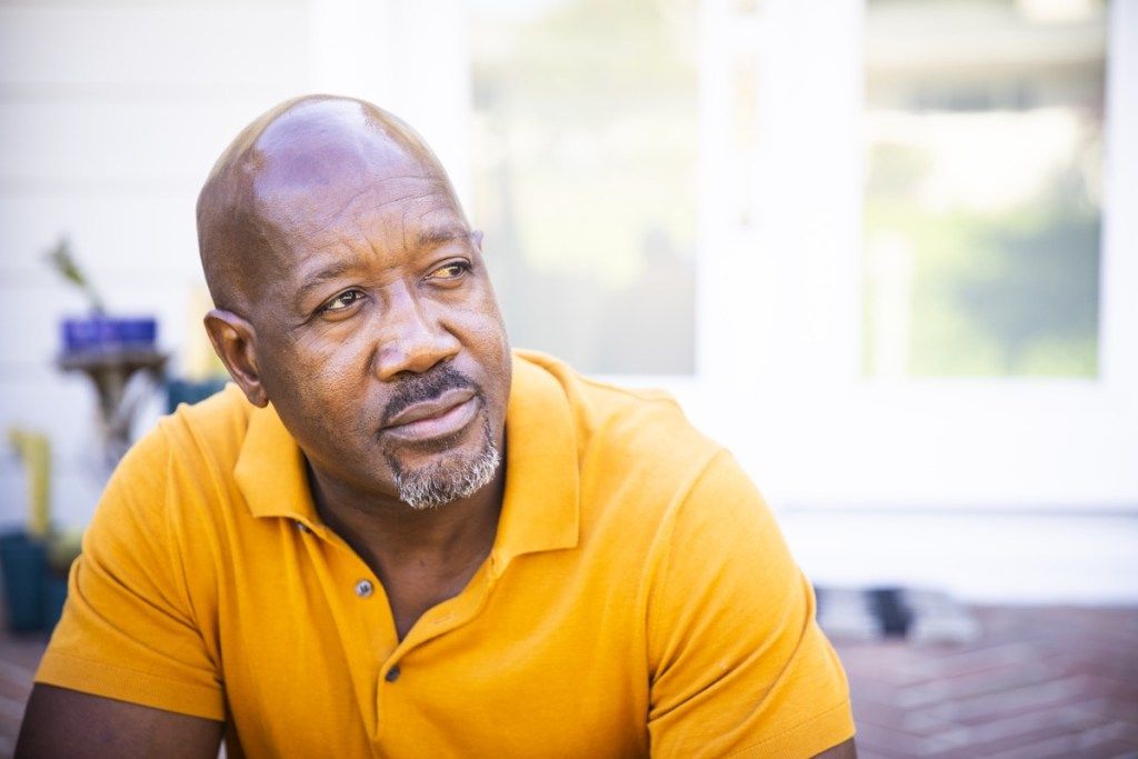 Seorang pria kulit hitam dewasa melihat keluar sambil duduk di teras rumahnya