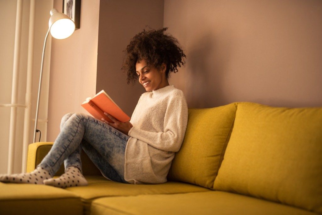 Sieviete lasot grāmatu uz dīvāna